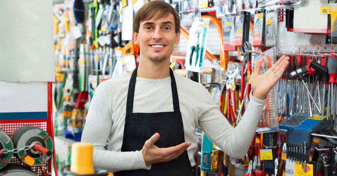 Hardware store worker gesturing towards assorted tools behind counter