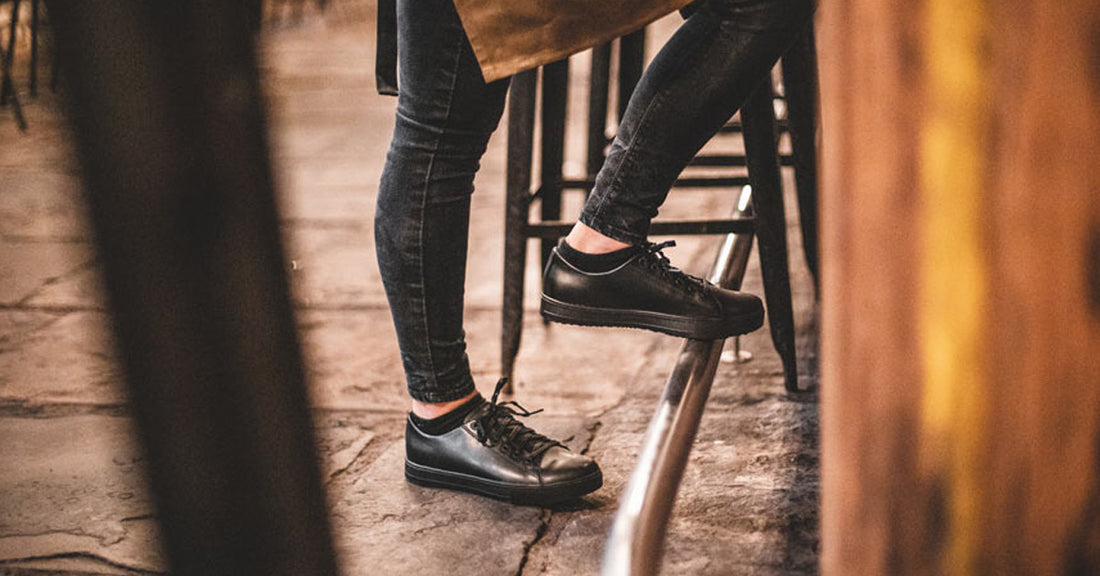 Woman wearing black slip-resistant restaurant shoes with foot balancing on metal bar