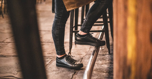 Woman wearing black slip-resistant restaurant shoes with foot balancing on metal bar