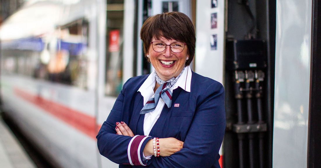 Female public transport employee smiling with arms crossed and standing next to train on platform