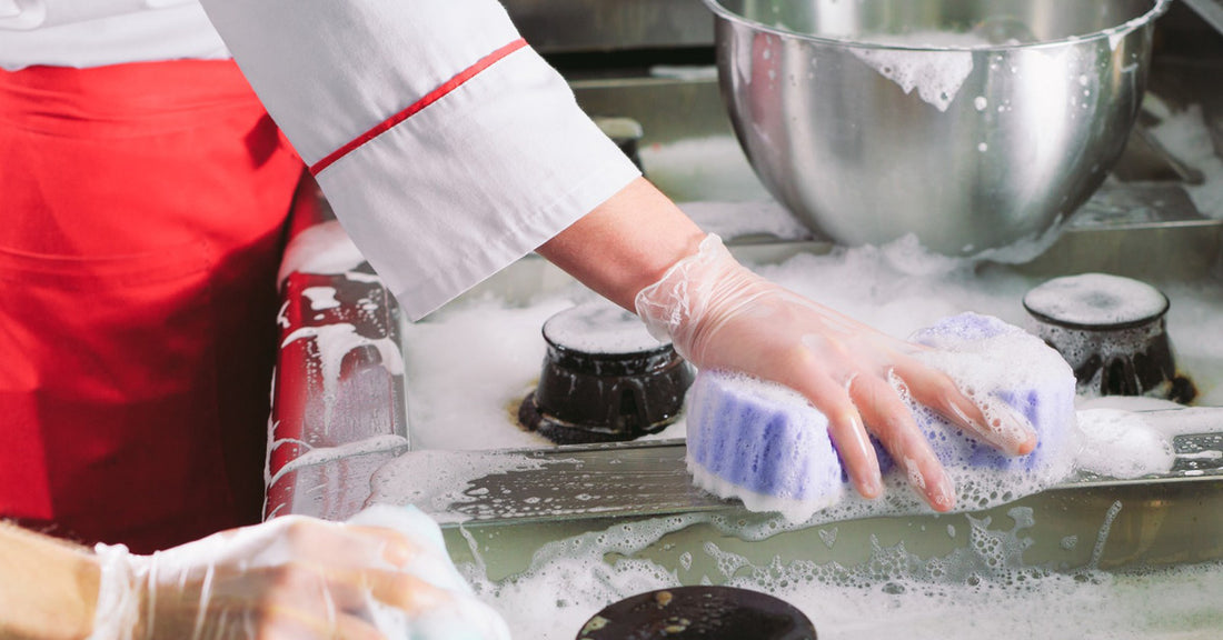 Two chefs cleaning the industrial-sized stove inside a restaurant with chemicals