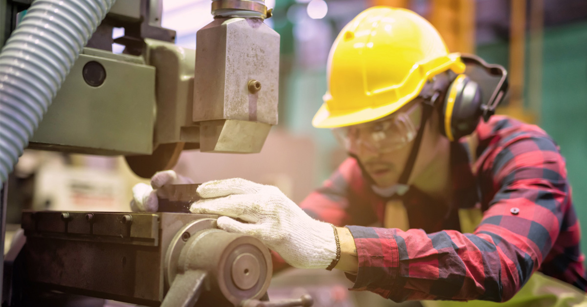Un hombre, protegido con casco, guantes y orejeras, trabaja con una máquina en una fábrica