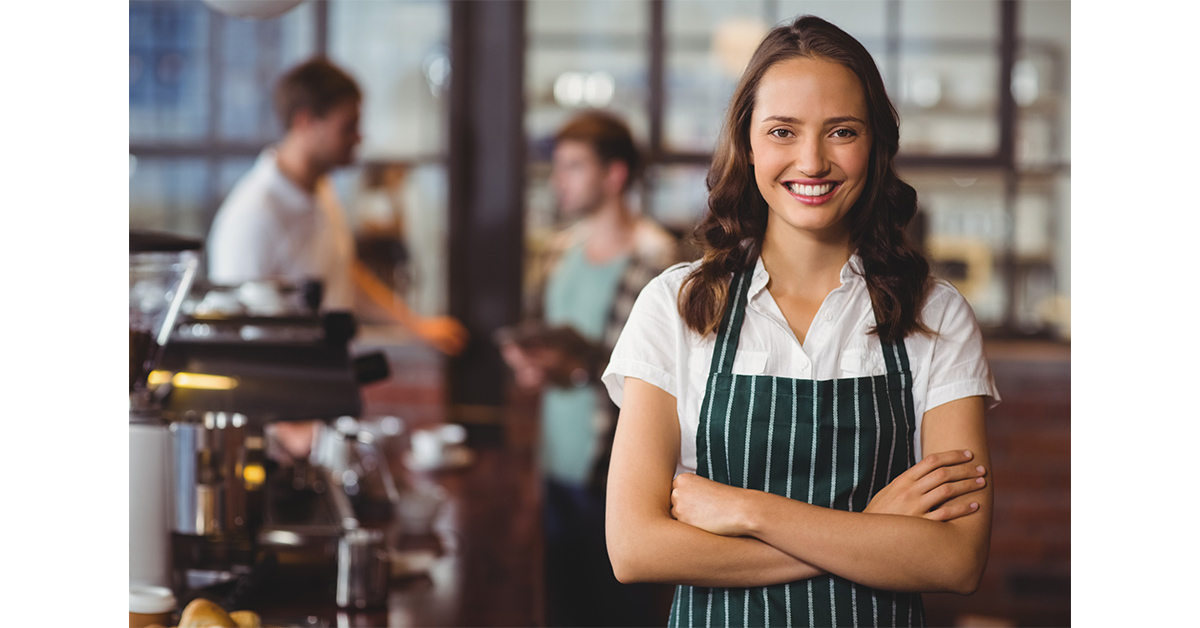 Una camarera sonríe a la cámara en el comedor de un restaurante con los clientes al fondo