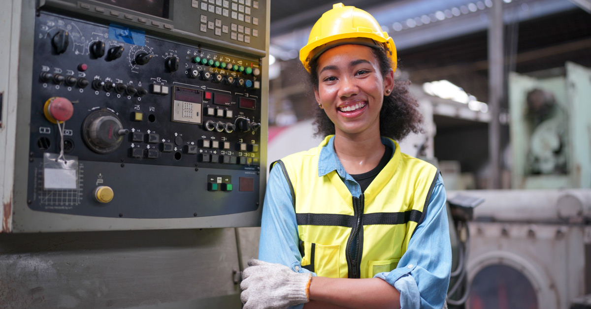 Smiling engineer wearing PPE in a manufacturing plant and standing next to a machine
