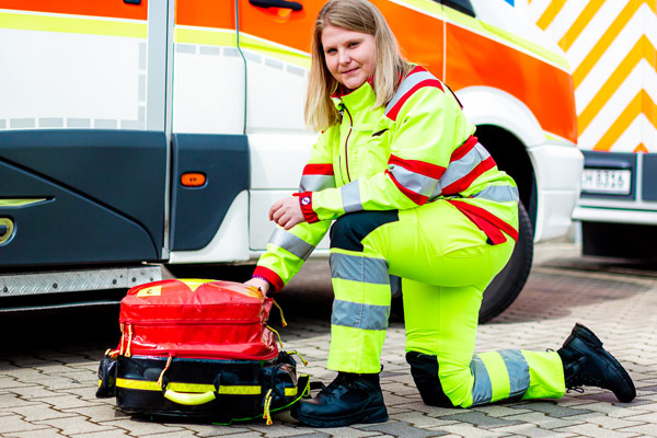 Paramedic kneeling down on ground next to ambulance preparing emergency kits