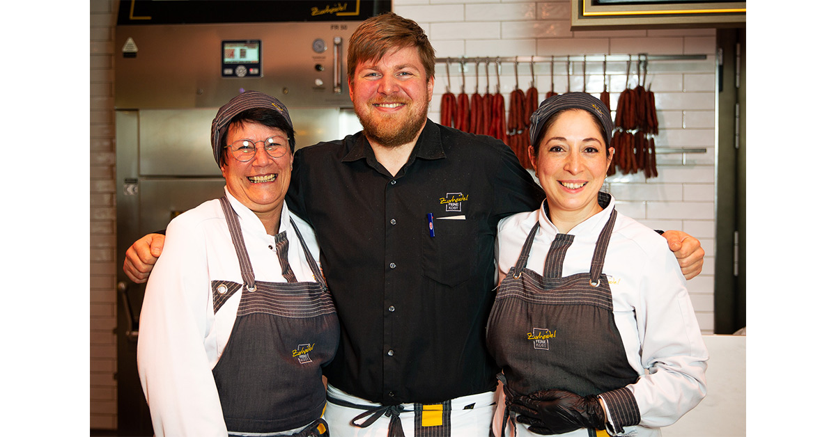 Group of three staff members smiling and standing behind butcher’s counter